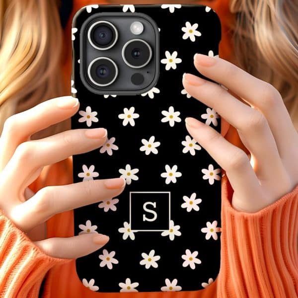 A Woman'S Hands Hold A Black Phone Case Covered In Small White Daisies And A White Square With The Letter S In The Center.