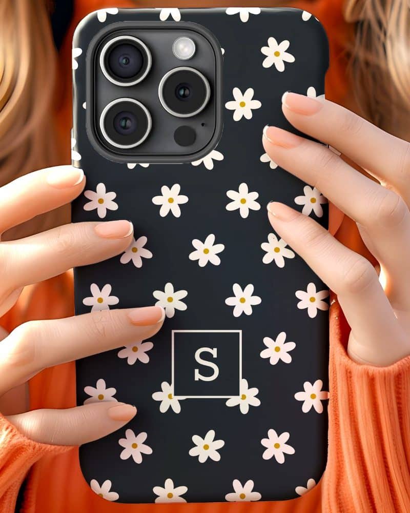 Close-up of hands holding a dark phone case decorated with white daisies and a white letter S.