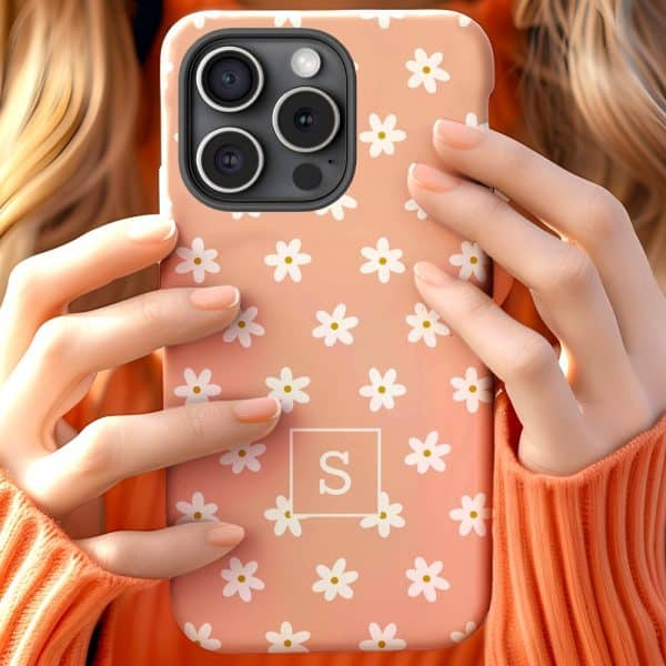 Close-Up Of Hands Holding A Peach-Colored Phone Case With White Daisies And A Monogram.