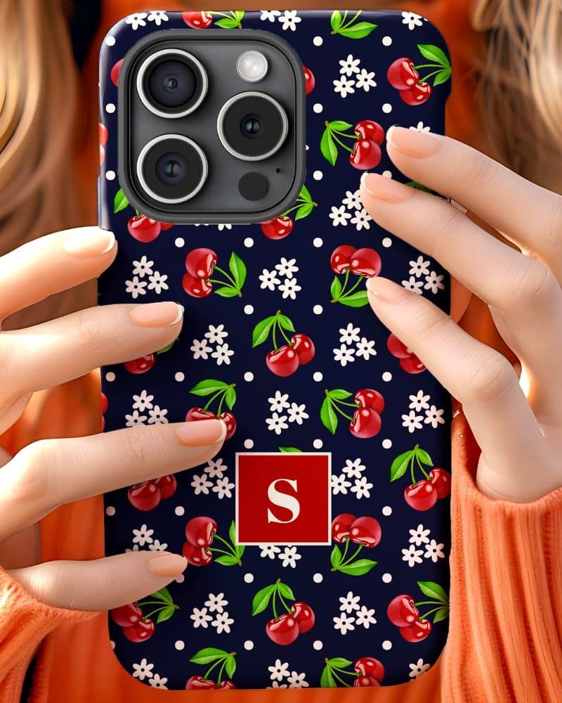 Woman's hands holding a navy blue phone case with a cherry and floral pattern and a red S initial.