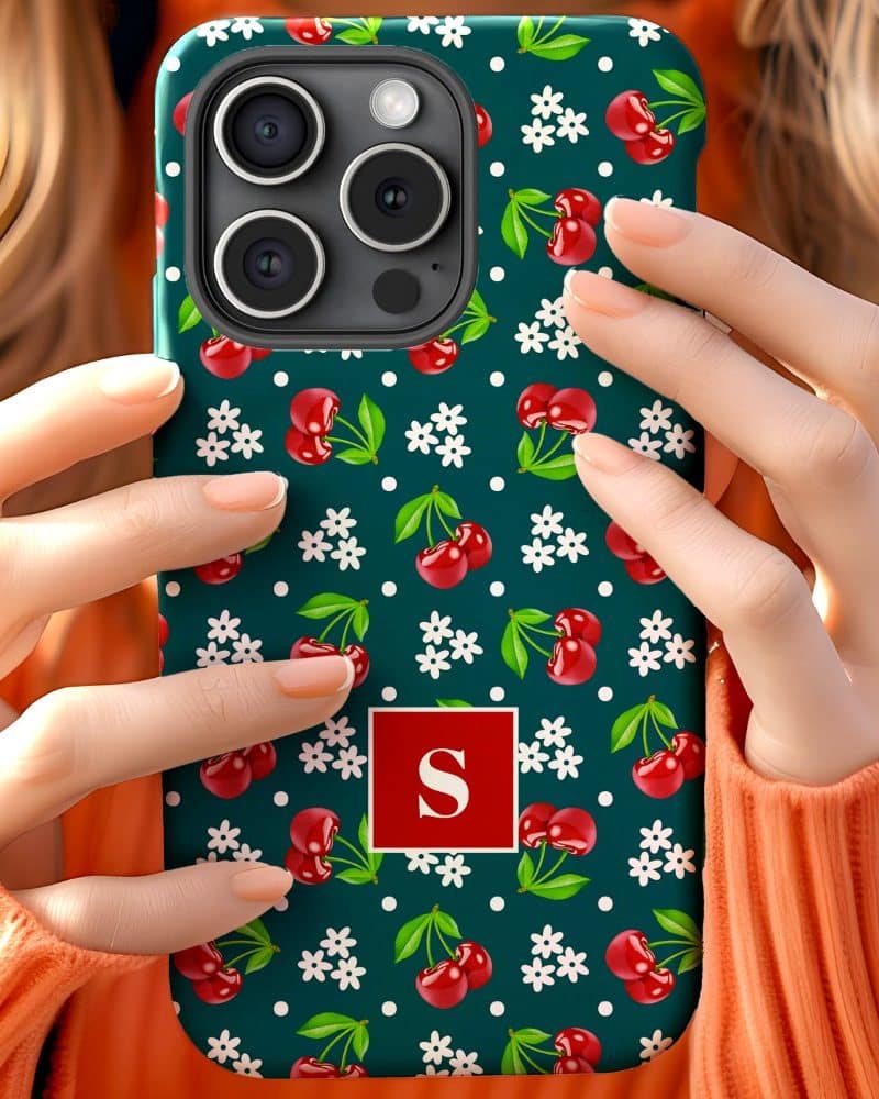 Hands holding a teal phone case with a cherry and flower pattern and a red square with the letter S.