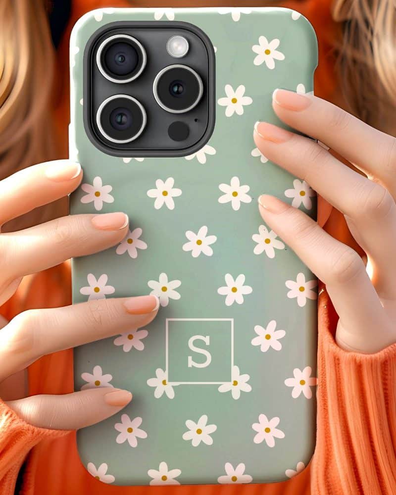 Hands holding a light green phone case decorated with small white daisies and a white square with the letter S.