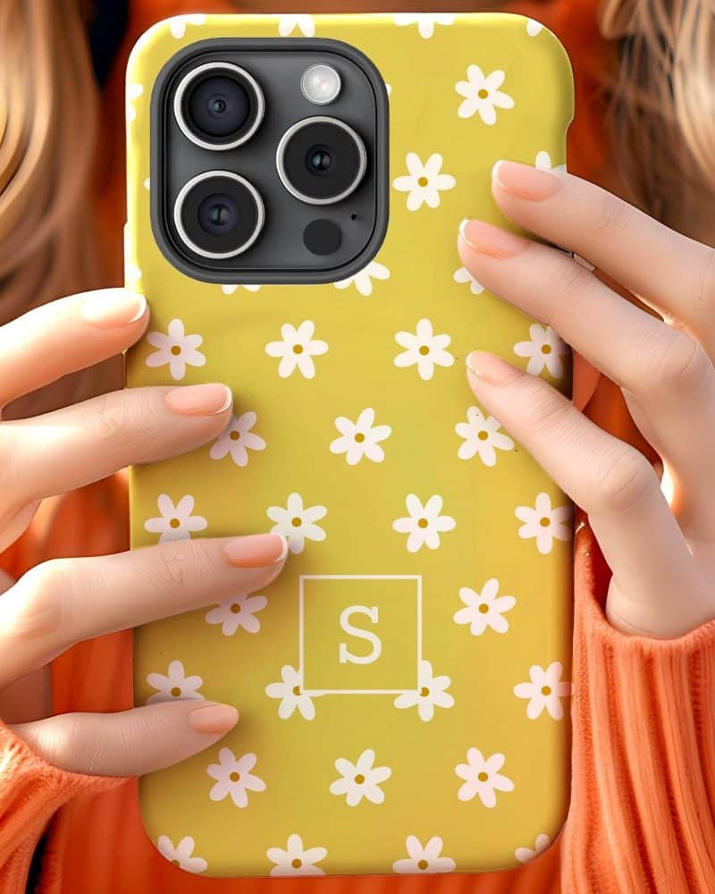 Hands holding a yellow iPhone case with a white daisy pattern and the letter S in a white square.