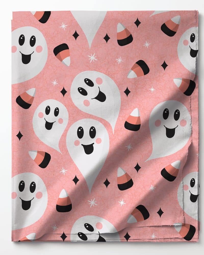 Pink fabric with a repeating pattern of smiling ghosts and candy corn.