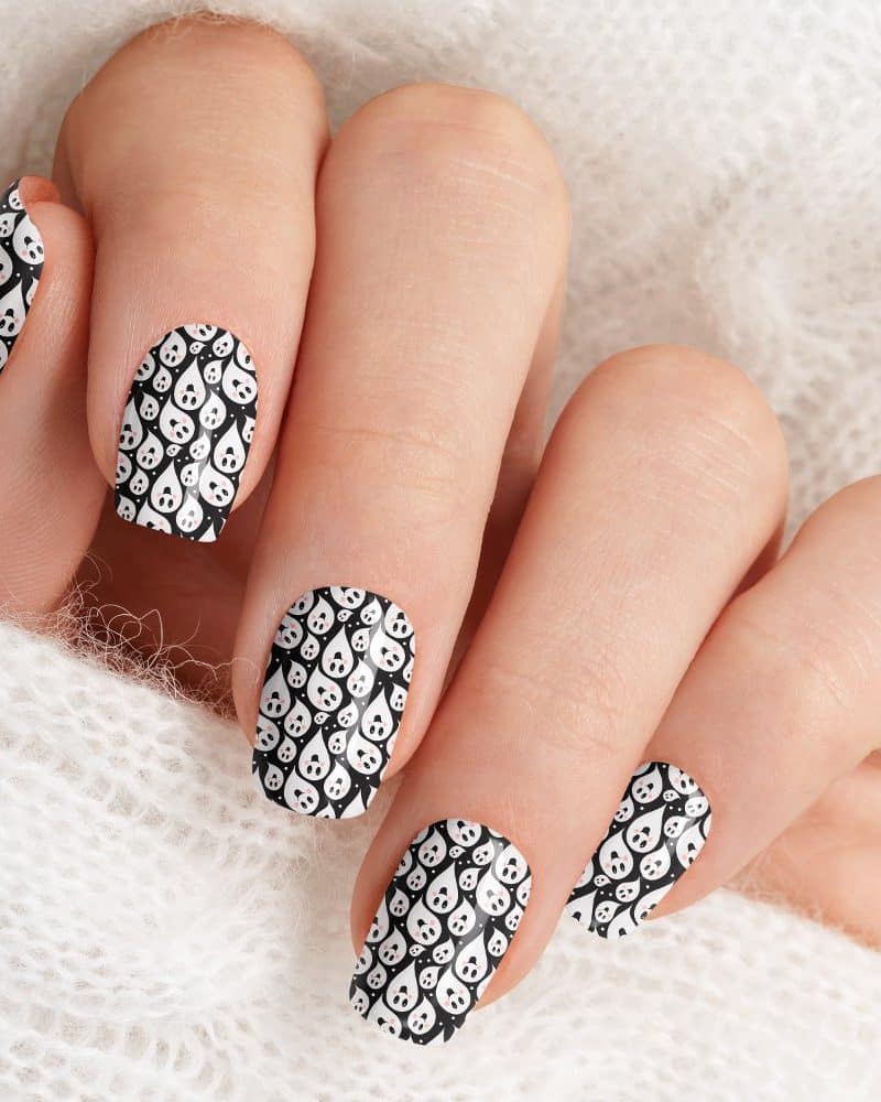 Close-up of a hand with fingernails decorated with a black and white ghost pattern.