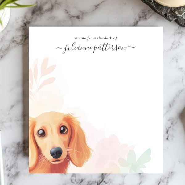 A Tan Longhaired Dachshund'S Head And Shoulders Peek From Behind Pastel Flowers On A Personalized Notepad.