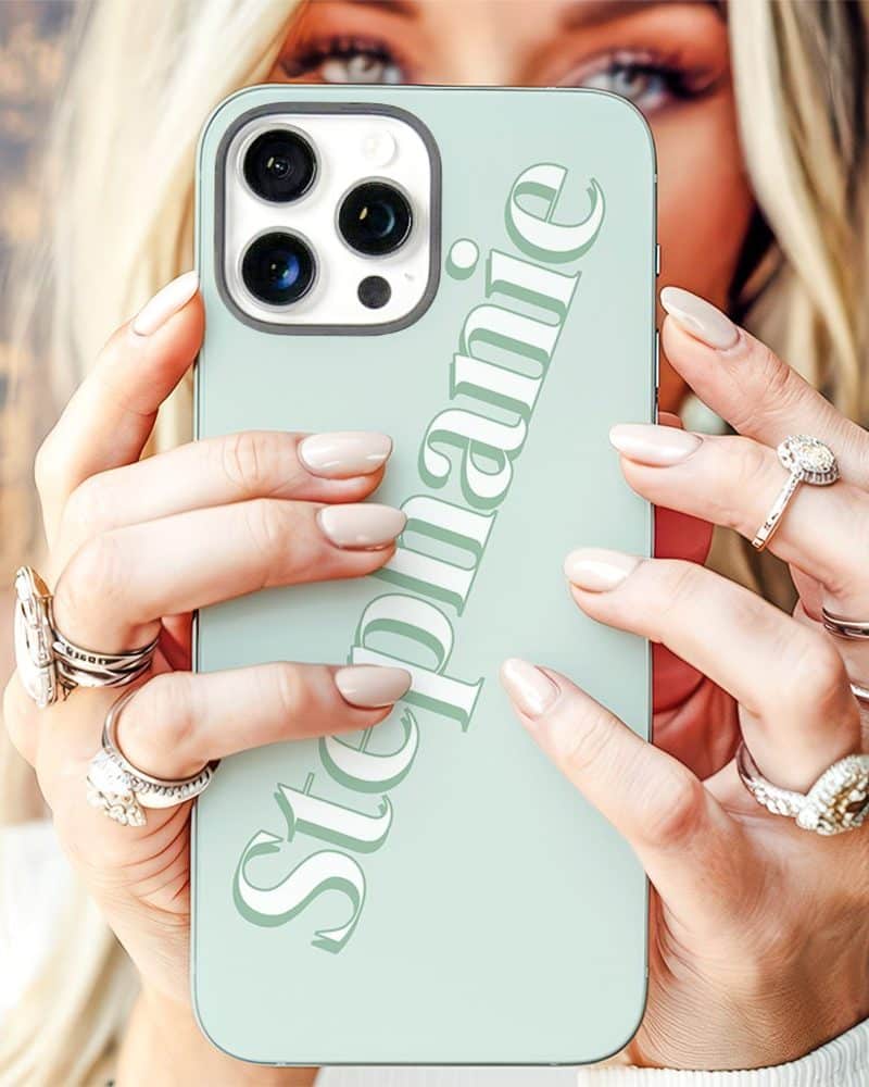 Close-up of a woman's hands holding a light green iPhone case with the name Stephanie printed on it.