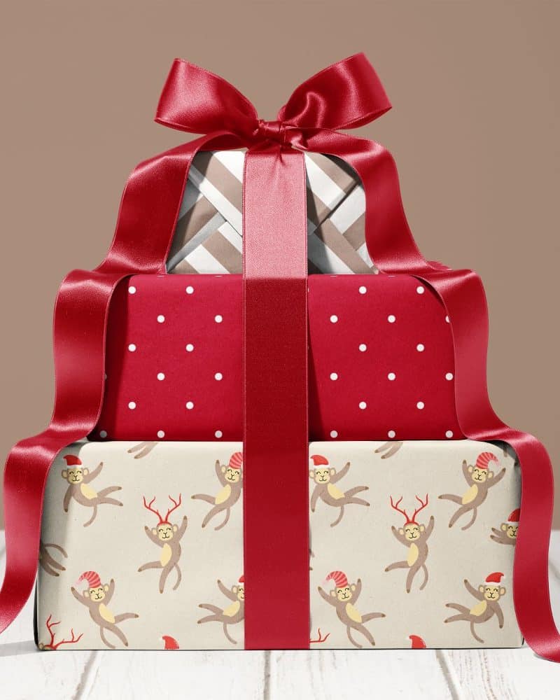 Stack of three Christmas presents tied with a large red ribbon. The bottom present features a pattern of monkeys wearing Santa hats.