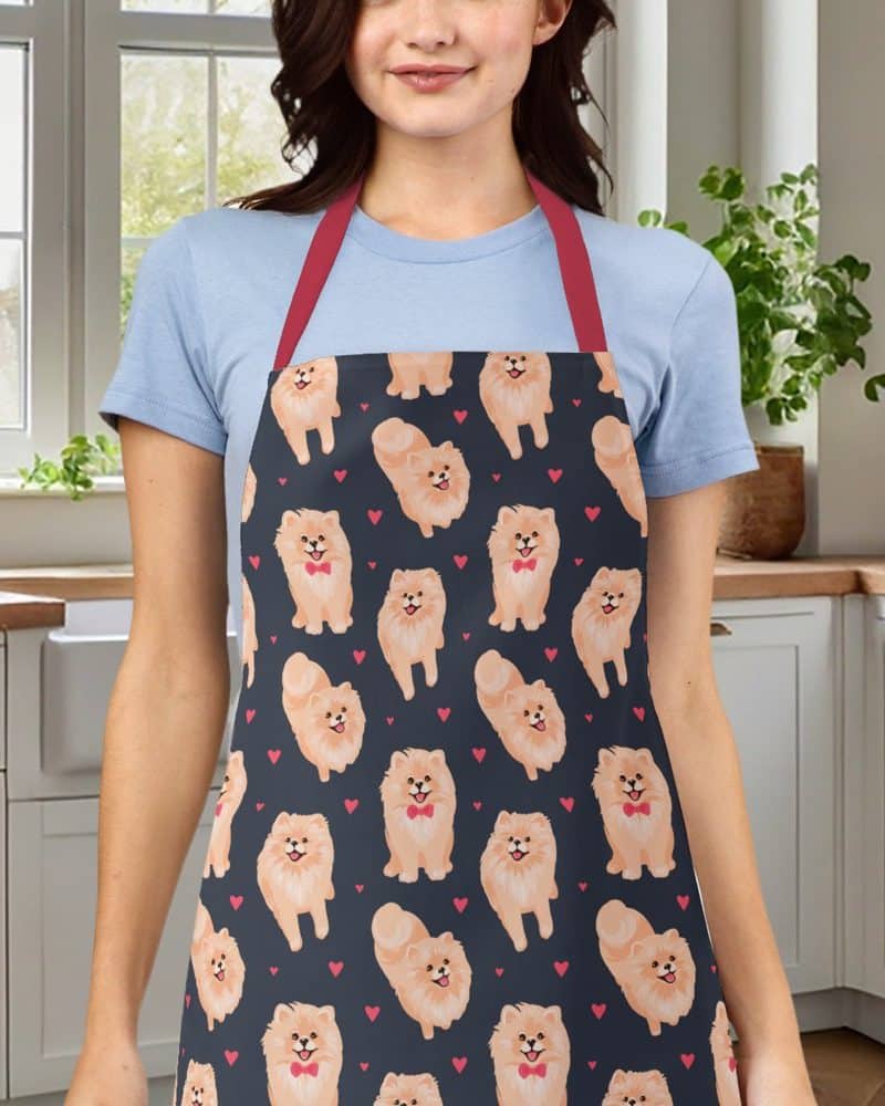 Woman wearing a dark apron with a repeating pattern of Pomeranian dogs and red hearts.