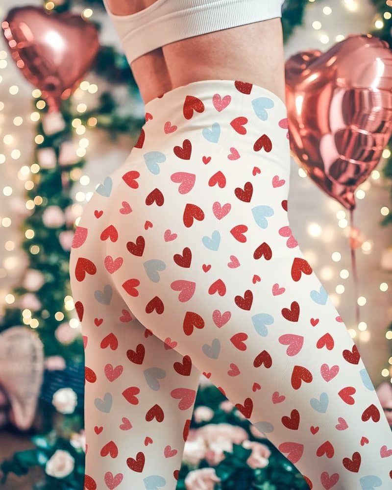 The lower half of a person wearing cream-colored leggings patterned with small red, pink, and light blue hearts.