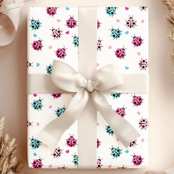 Gift Wrapped In White Paper With A Repeating Pattern Of Pink, Blue, And Black Ladybugs And Small Hearts. A Beige Ribbon Is Tied In A Bow On Top.