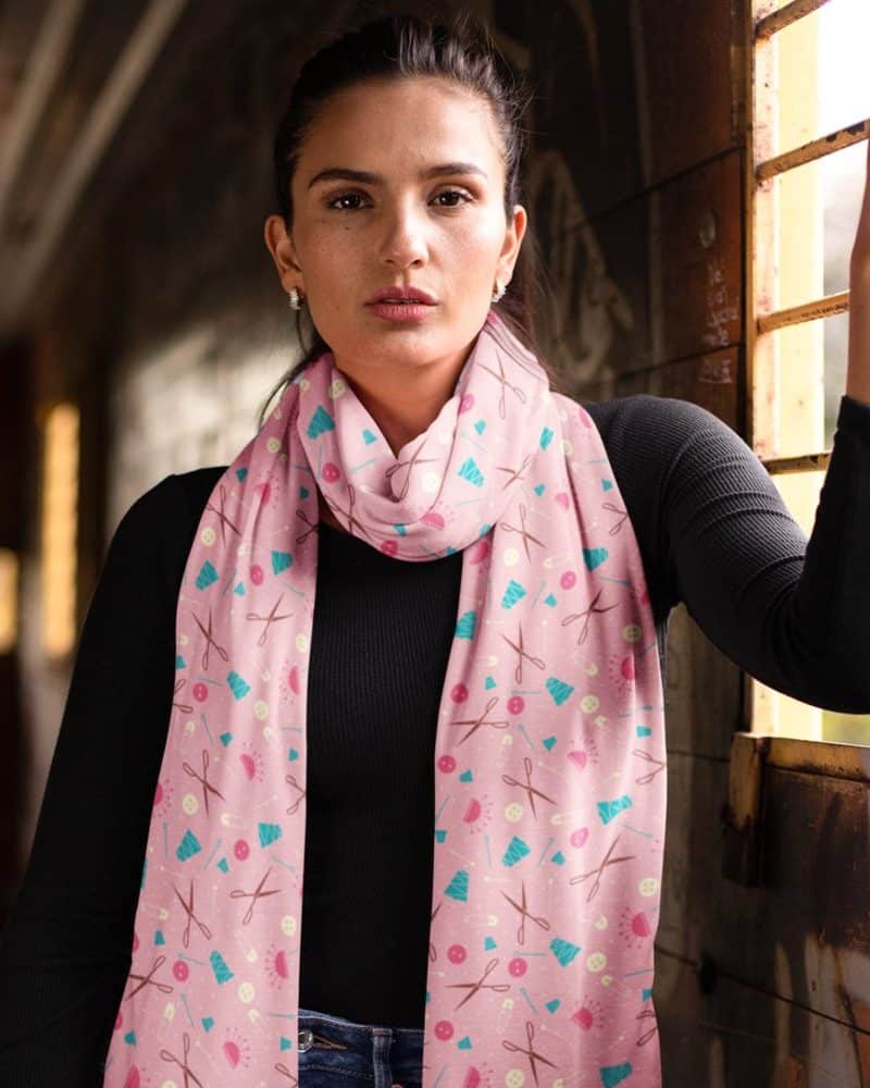 Woman wearing a pink scarf with a sewing theme pattern.