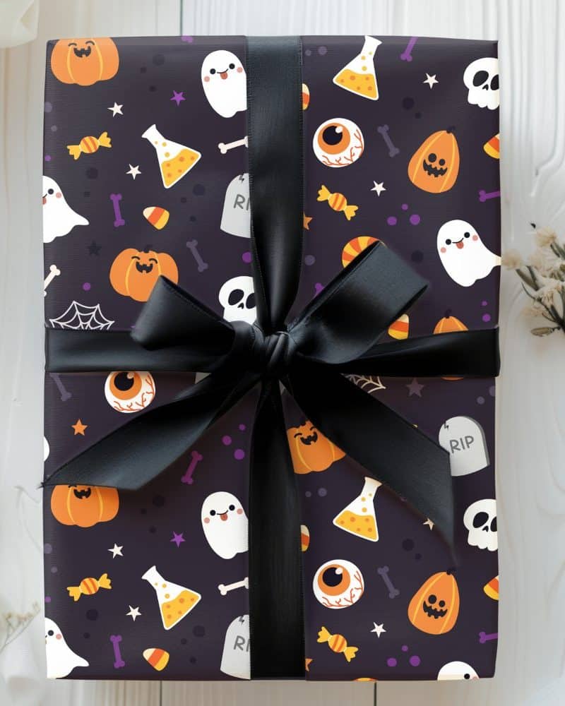 Halloween gift wrapped in dark purple paper with a black ribbon. The paper features a pattern of cartoon pumpkins, ghosts, eyeballs, and candy corn.