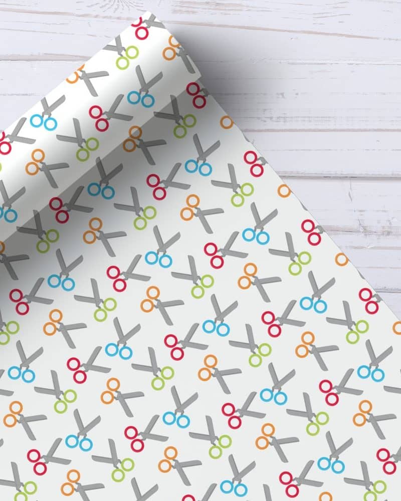 Partially rolled wrapping paper with a repeating pattern of grey scissors and colorful rings.