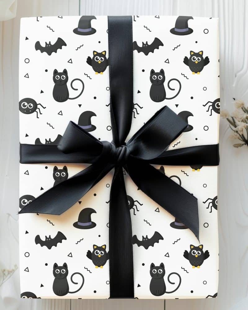 Halloween gift wrapped in black and white paper featuring black cats, bats, owls, and spiders.