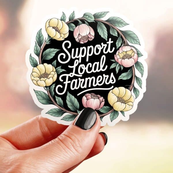 A Hand Holds A Round Sticker With A Floral Wreath Surrounding The Text Support Local Farmers.