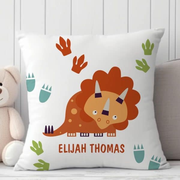 White Pillow With A Cartoon Triceratops, Dinosaur Footprints, And The Name Elijah Thomas.
