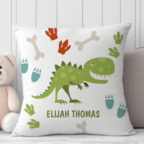 White Pillow With A Green Dinosaur, Dinosaur Footprints, And Bones. The Name Elijah Thomas Is Printed Below The Dinosaur.