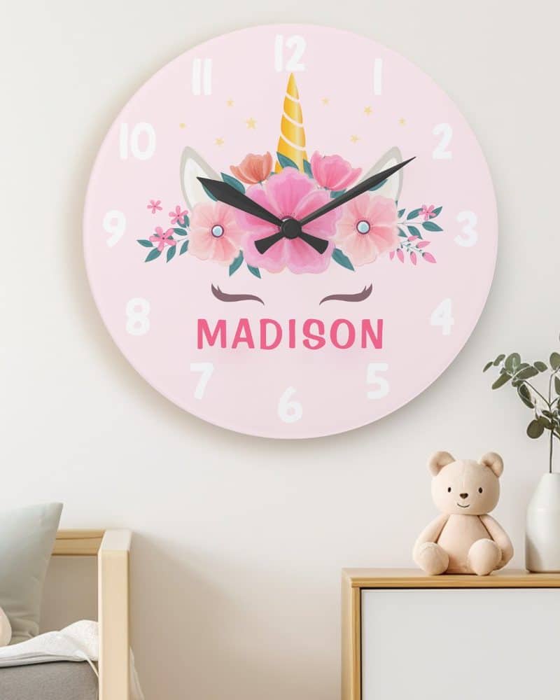 Pink children's wall clock featuring a unicorn face with flowers and the name Madison.