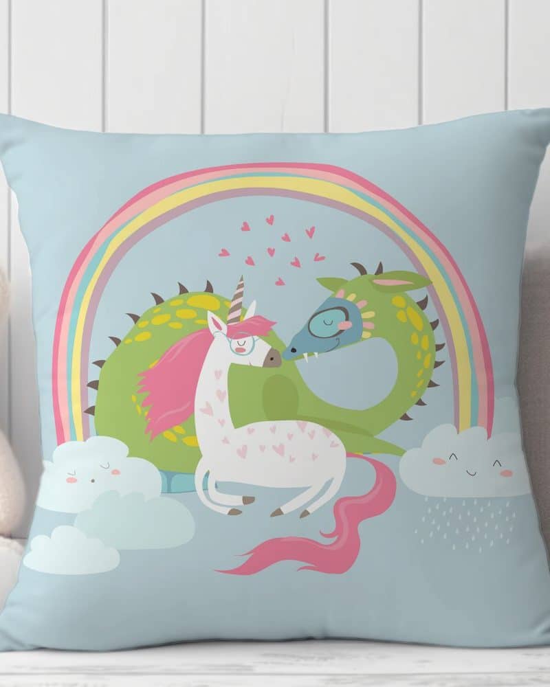 Light blue pillow with a unicorn and dragon nuzzling under a rainbow.