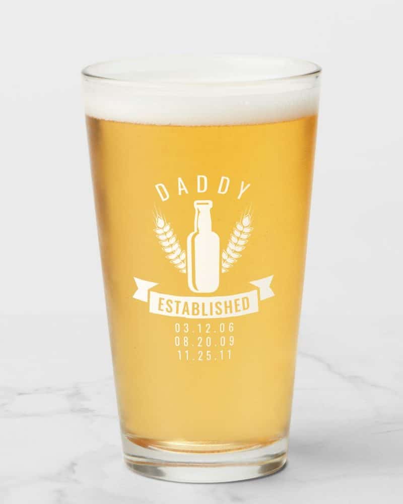 A pint glass of beer with a design that says Daddy Established and lists three dates.