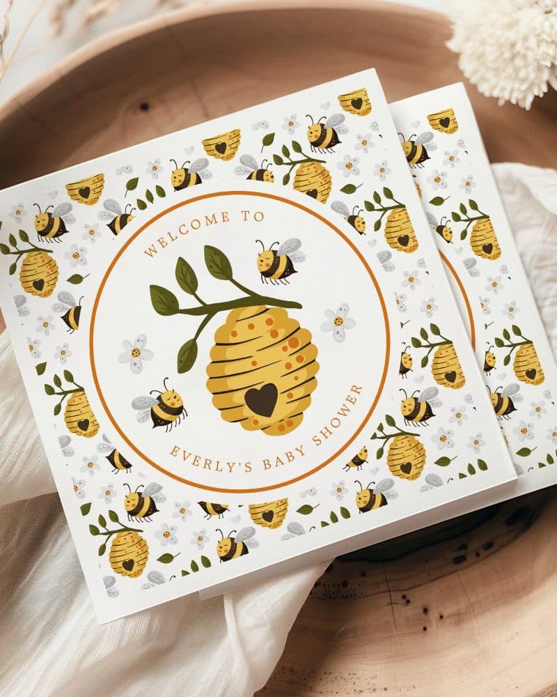 Baby shower invitation featuring a beehive with bees and flowers.