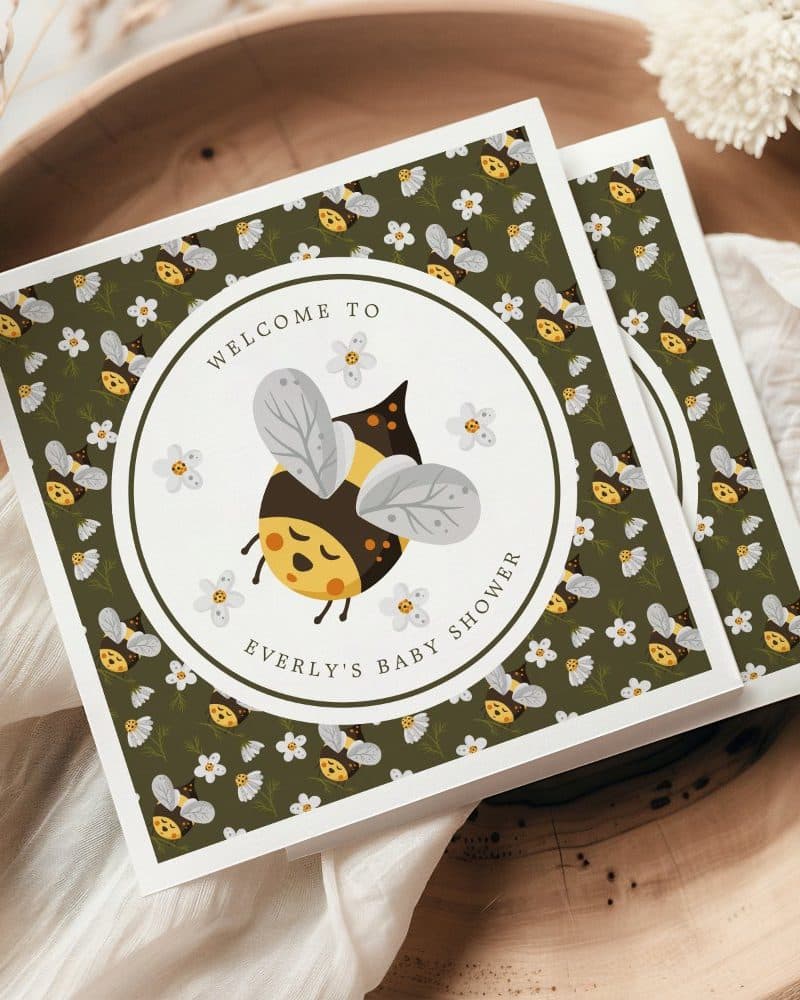 Baby shower invitation featuring a cartoon bee and floral pattern.