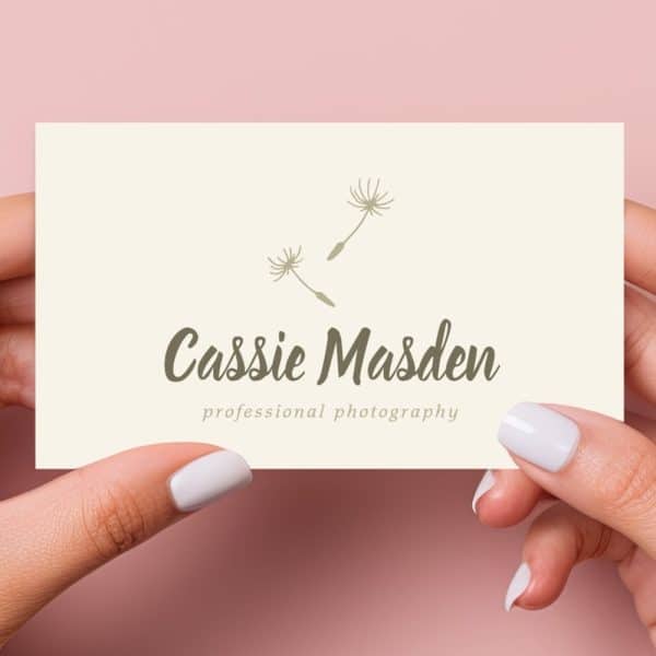 Two Hands Hold A Cream-Colored Business Card Featuring The Name Cassie Marsden And The Words Professional Photography, Along With A Simple Dandelion Seed Design.