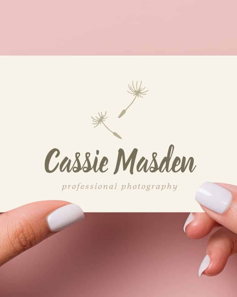 Two hands hold a cream-colored business card featuring the name Cassie Marsden and the words professional photography, along with a simple dandelion seed design.