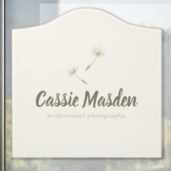 Off-White Sign With Arched Top, Featuring The Name Cassie Madsen And Professional Photography Underneath, With Two Small Dandelion Seed Designs Above The Text.