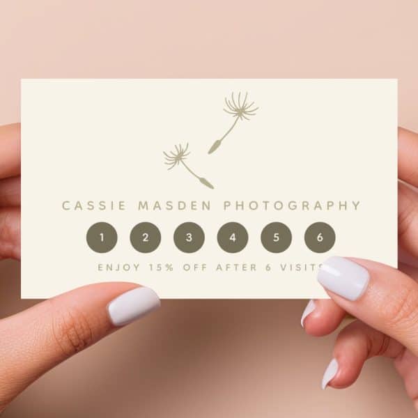 Hands Holding A Cassie Masden Photography Loyalty Card Featuring Two Dandelion Illustrations And Six Visit Spaces; 15% Off After Six Visits.