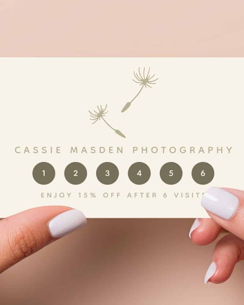 Hands holding a Cassie Masden Photography loyalty card featuring two dandelion illustrations and six visit spaces; 15% off after six visits.