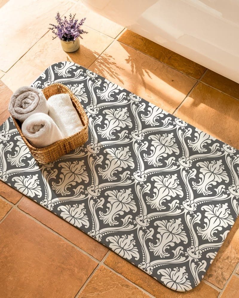 Dark gray bath mat with a beige damask pattern, featuring a wicker basket of rolled-up towels.