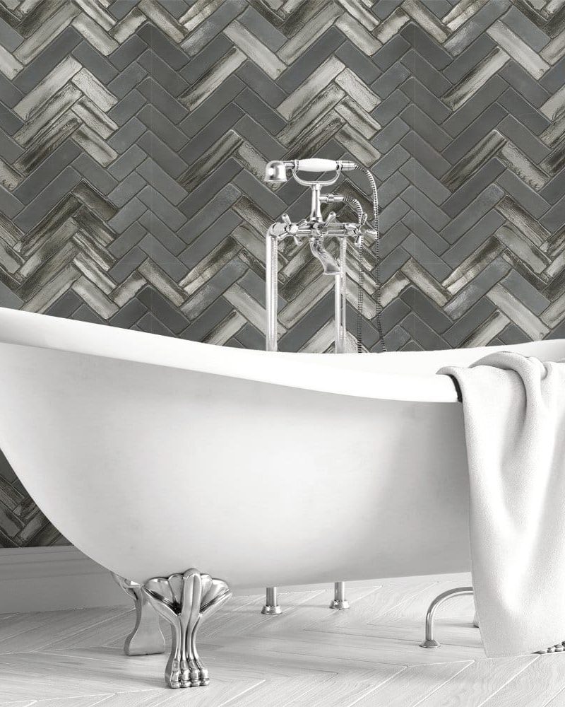 White clawfoot bathtub in front of a gray herringbone tile wall.
