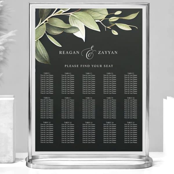 A Dark-Colored Wedding Seating Chart With Greenery Accents, Displaying Tables Numbered One Through Fifteen And Guest Names.