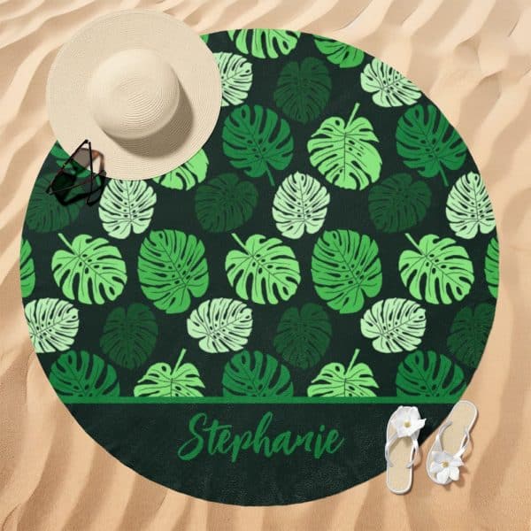 Round Beach Towel With A Dark Green Background And A Repeating Pattern Of Light And Dark Green Monstera Leaves. The Name Stephanie Is Printed Along The Bottom.