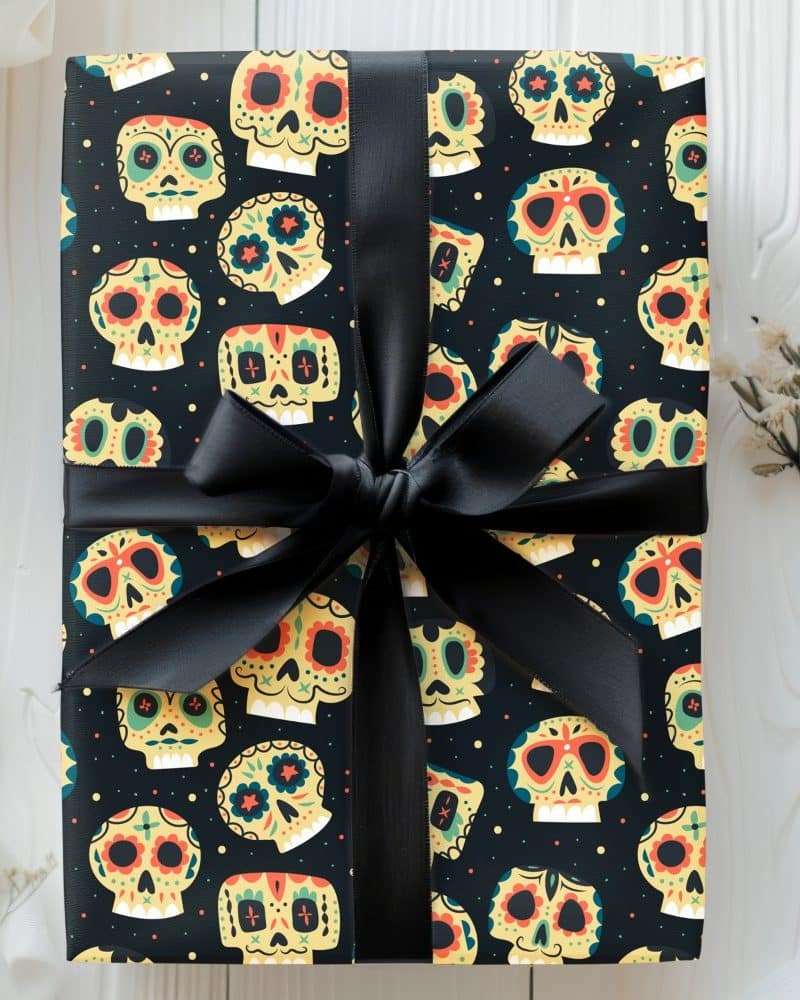 A gift wrapped in black paper featuring a repeating pattern of colorful sugar skulls, tied with a black ribbon.