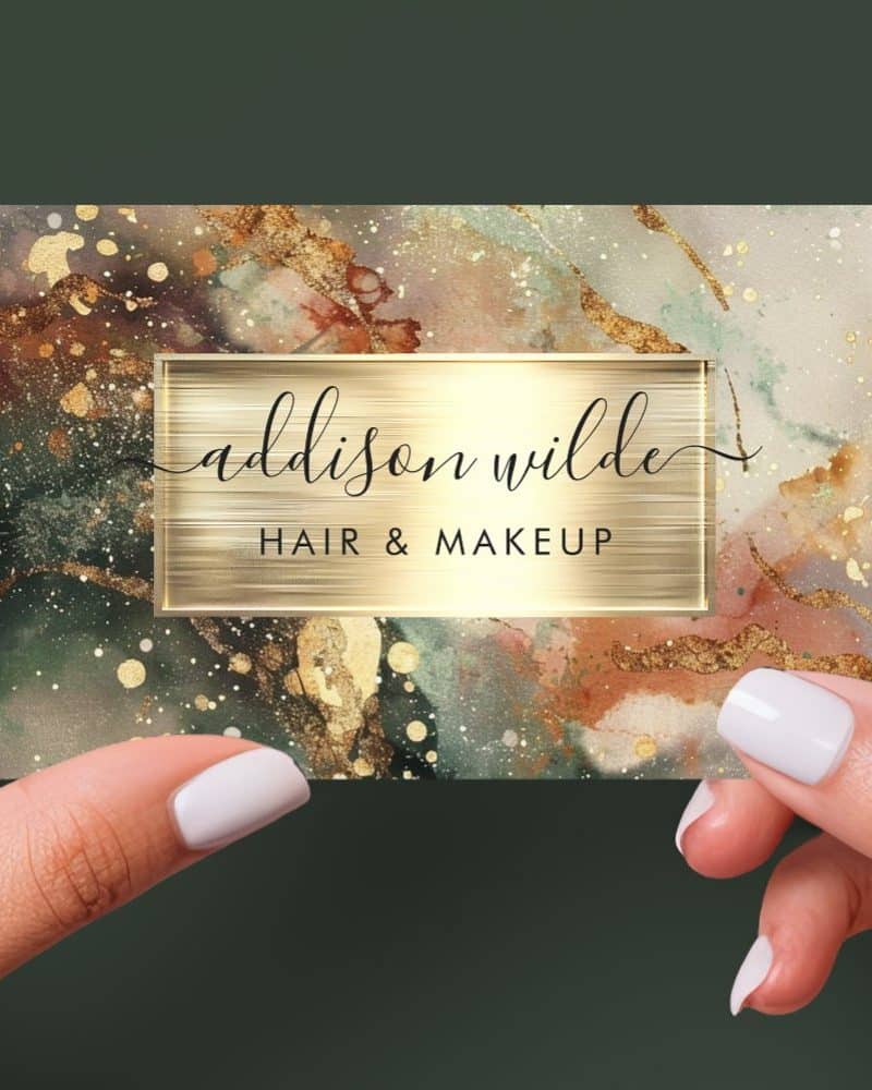 A business card for Addison Wilde Hair & Makeup, featuring an abstract watercolor design in gold, green, and brown tones.