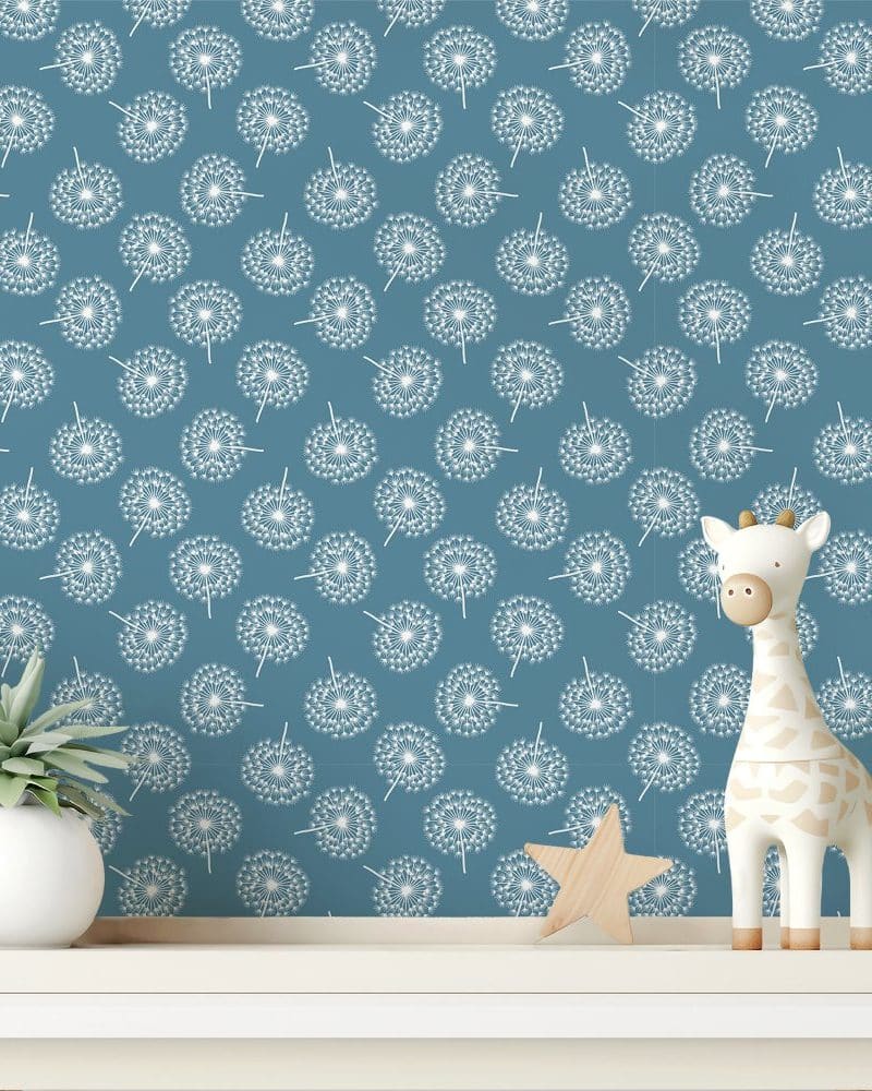 A teal wall with a repeating pattern of white dandelions, featuring a small wooden giraffe and plant on a shelf in front.