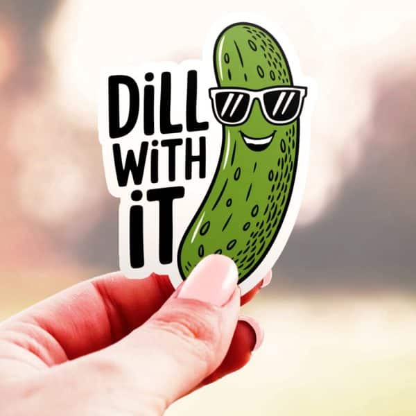 Hand Holding A Sticker Of A Smiling Pickle Wearing Sunglasses; Text On Sticker Says Dill With It.