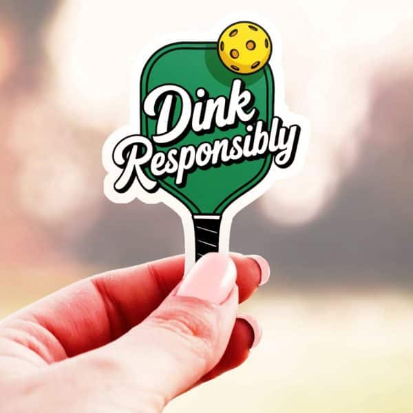 A Hand Holds A Sticker Of A Pickleball Paddle With The Text Dink Responsibly.