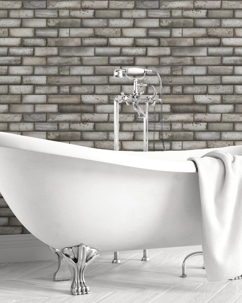 White clawfoot bathtub in front of a gray brick wall.