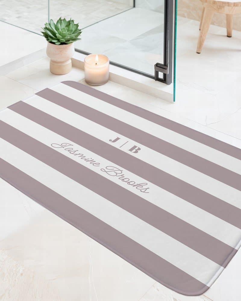 A mauve and white striped bath mat with the initials JB and the name Jasmine Brooks printed on it.