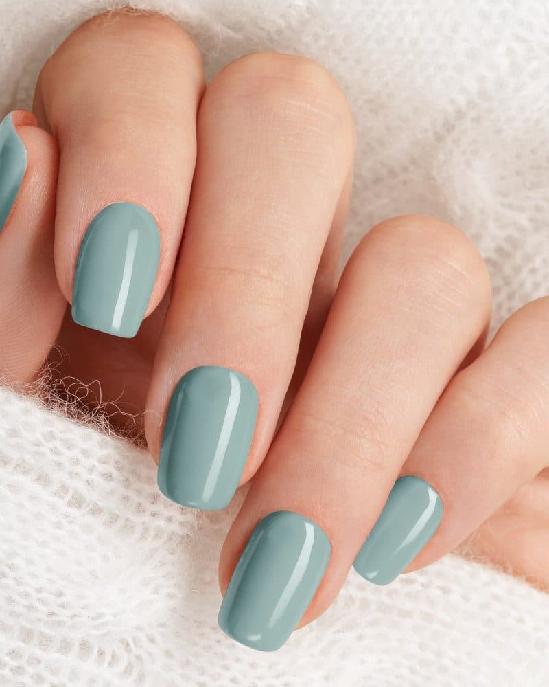 Close-up of a hand with pale blue painted nails resting on a white knit fabric.