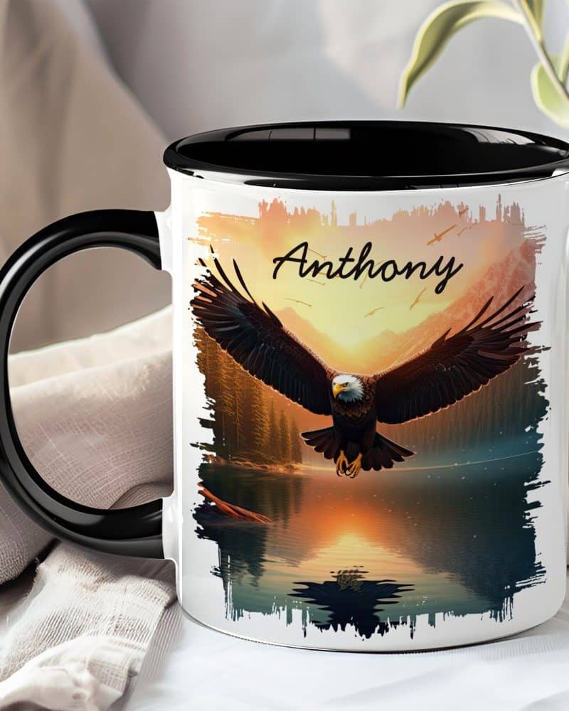 A black-handled mug with a personalized design featuring a bald eagle in flight over a sunset lake. The name Anthony is printed on the mug.
