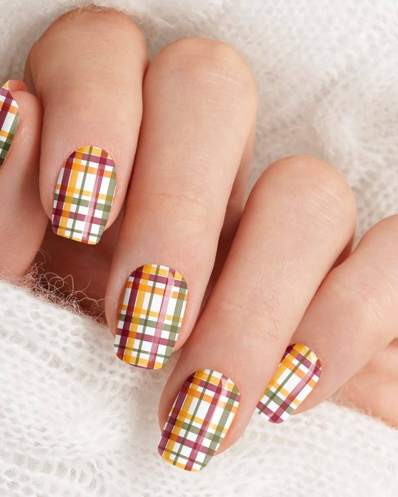 Hand with fingernails decorated with a plaid pattern in autumnal colors.