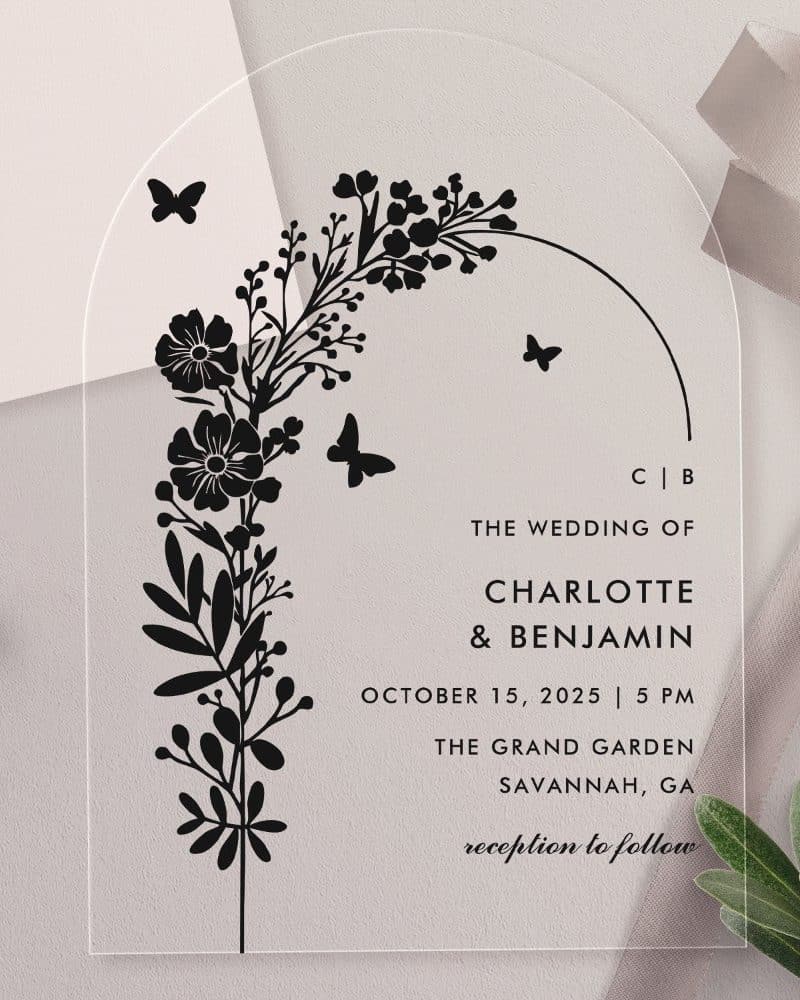 Clear acrylic wedding invitation with black floral design and wedding details.