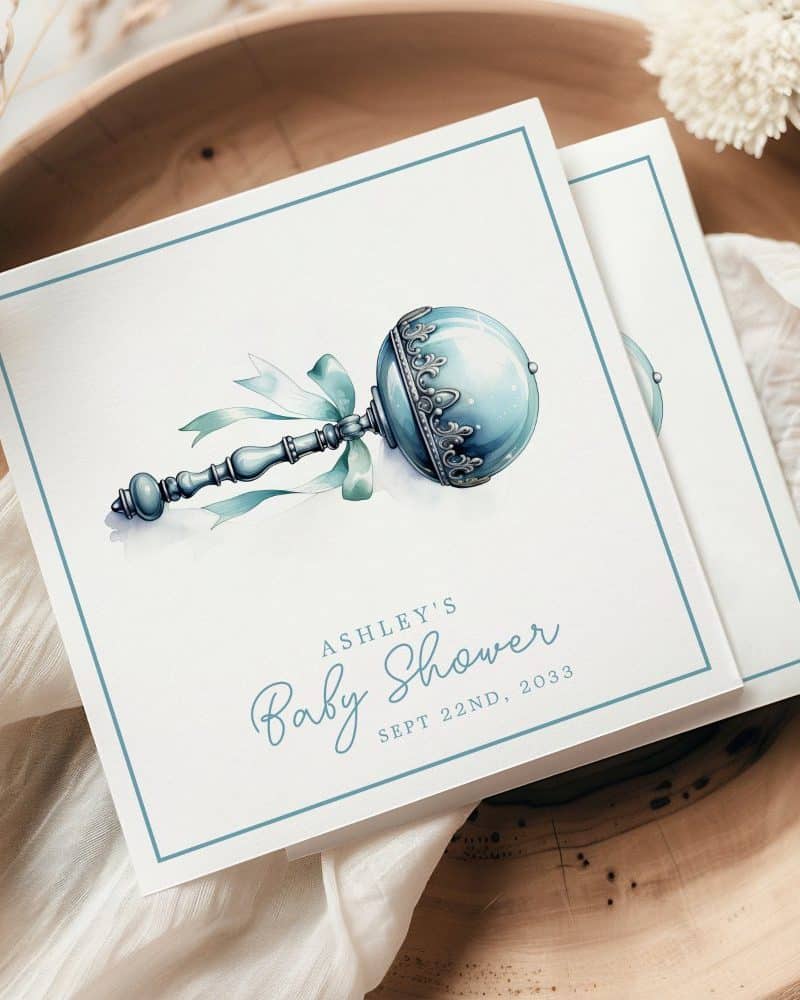 Baby shower invitation featuring a watercolor illustration of an ornate, blue rattle.