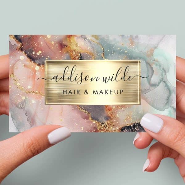 A Business Card For Addison Wilde Hair &Amp; Makeup, Featuring An Abstract Watercolor Design In Blush Pink, Gold, And Gray.