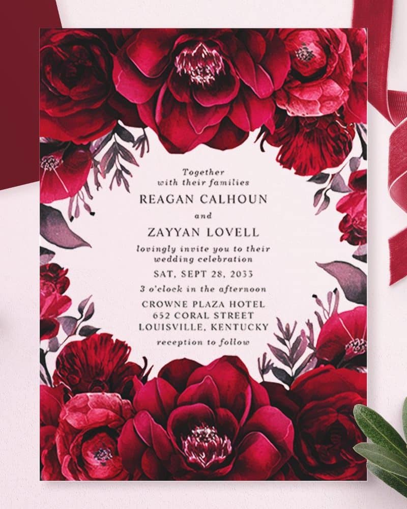 Wedding invitation with dark red floral border and text announcing the marriage of Reagan Calhoun and Zayyan Lovell.